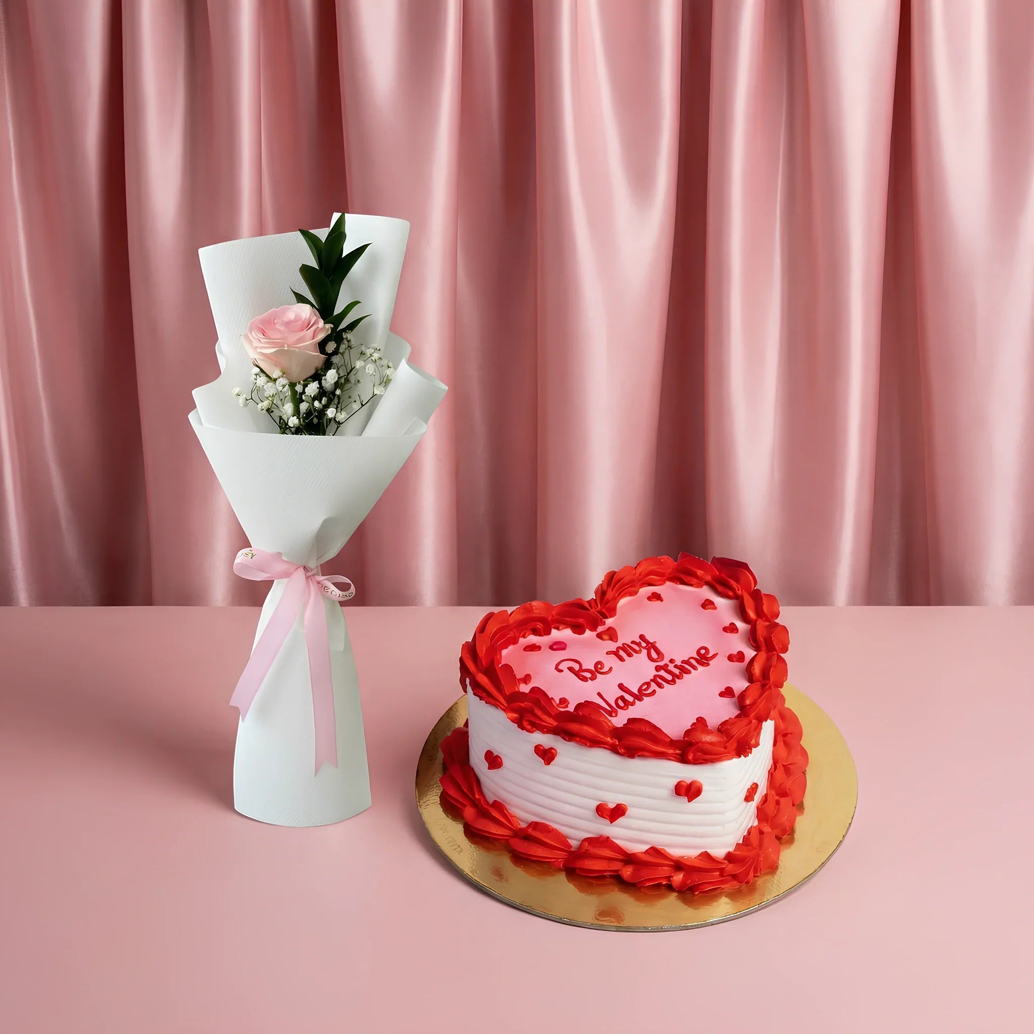 best valentine cake in dubai – heart-shaped red and white valentine’s cake with ‘be my valentine’ text, paired with a pink rose bouquet on a soft pink background.