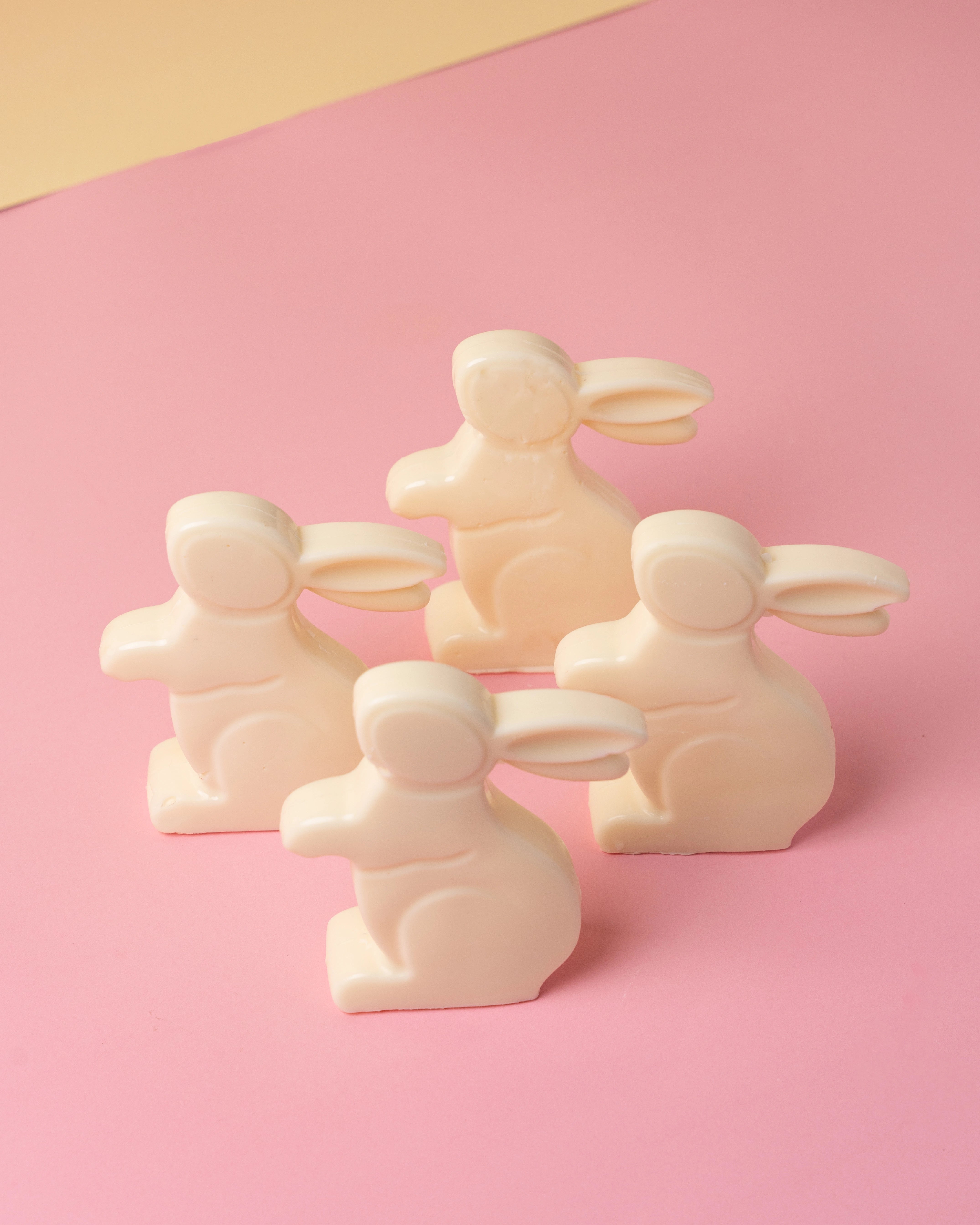 easter white chocolate bunny shapes with smooth finish arranged on pastel pink surface with soft yellow background, festive treats from red ribbon cakes & bistro dubai