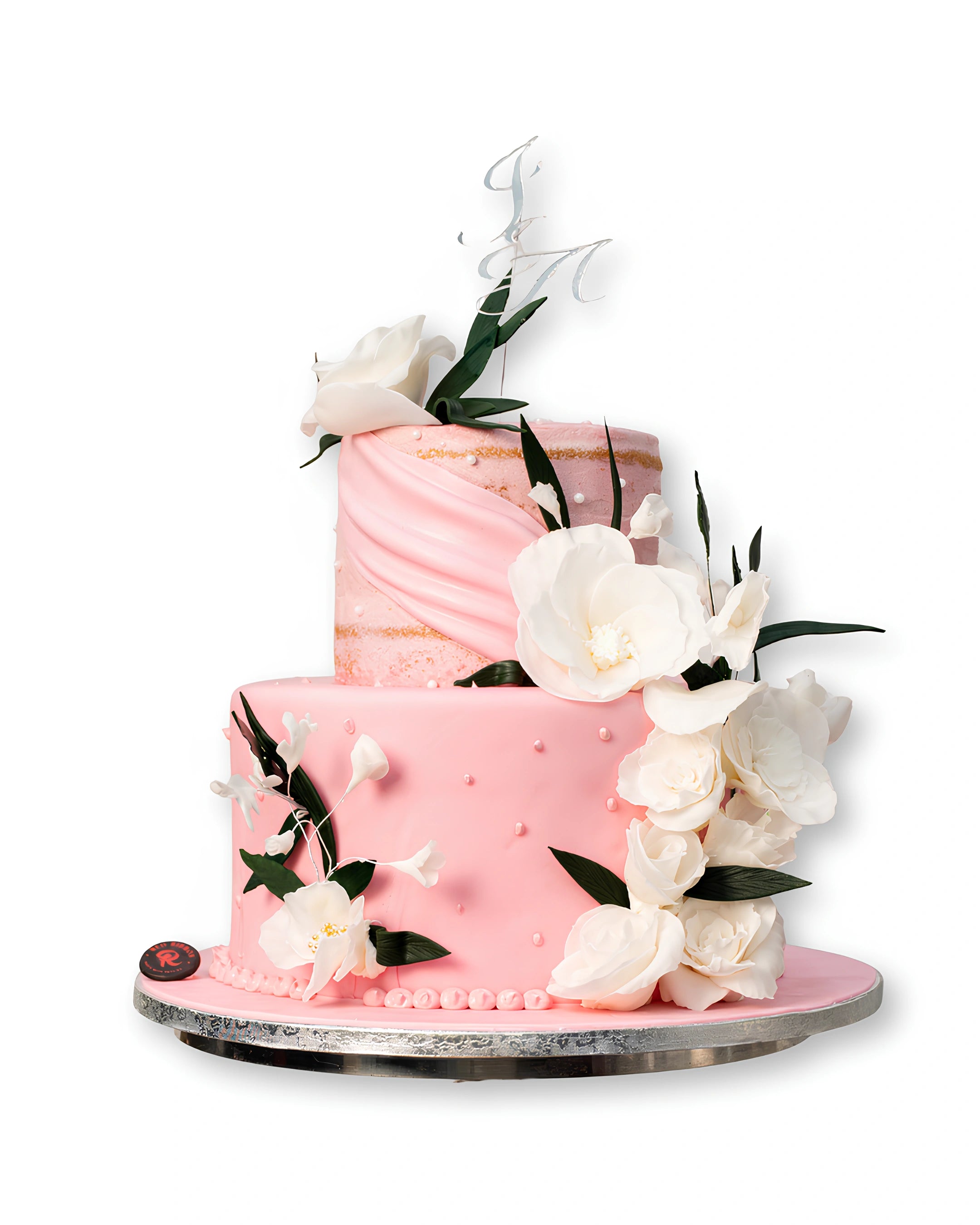 Blush pink two-tier wedding cake with white sugar flowers, soft draped buttercream texture, pearl details, and elegant floral arrangement on a silver cake stand