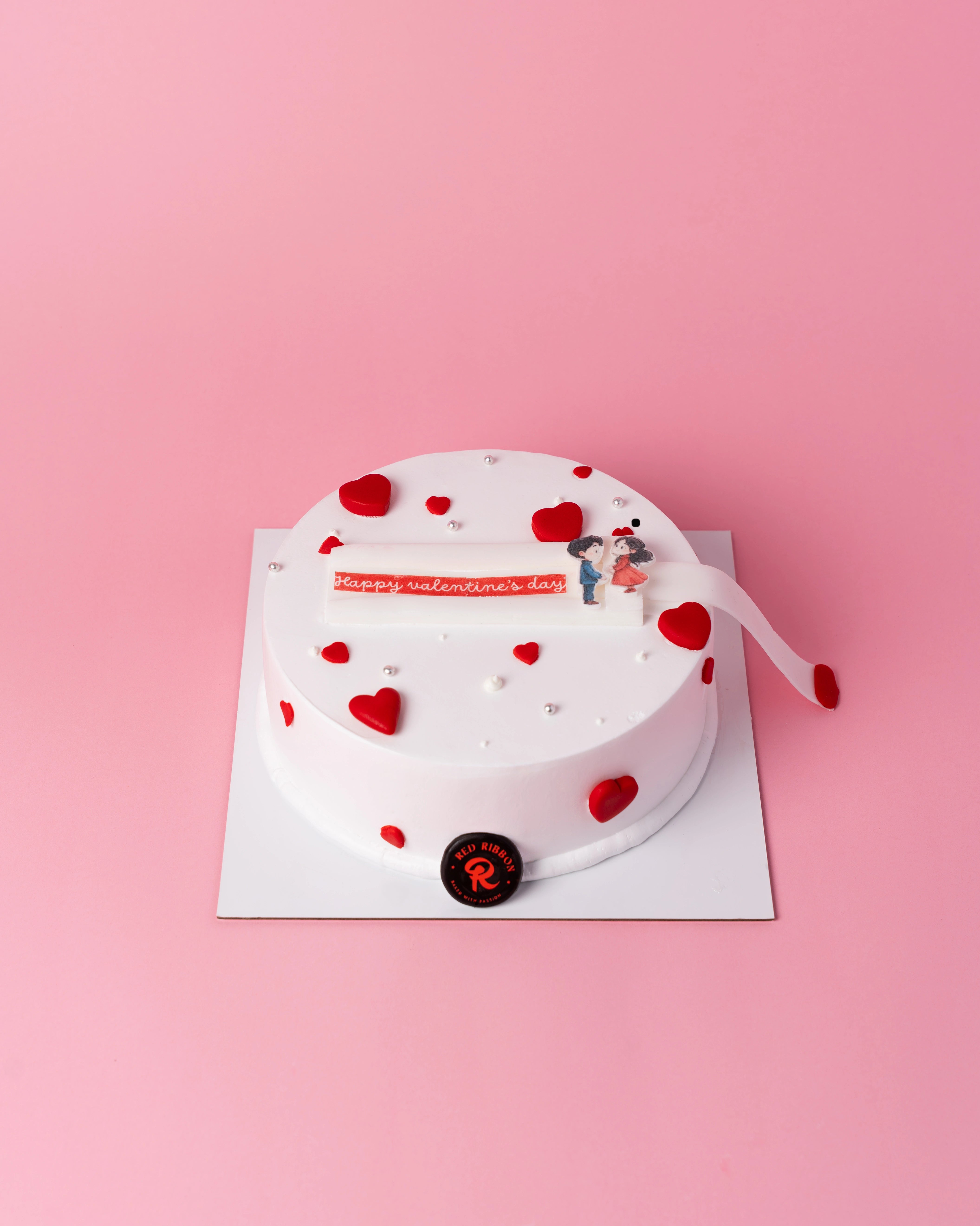 The Timeless Romance Cake from Red Ribbon, the best cake in Dubai for Valentine's Day, featuring a white frosted round design with red hearts and a romantic pull-tab message.