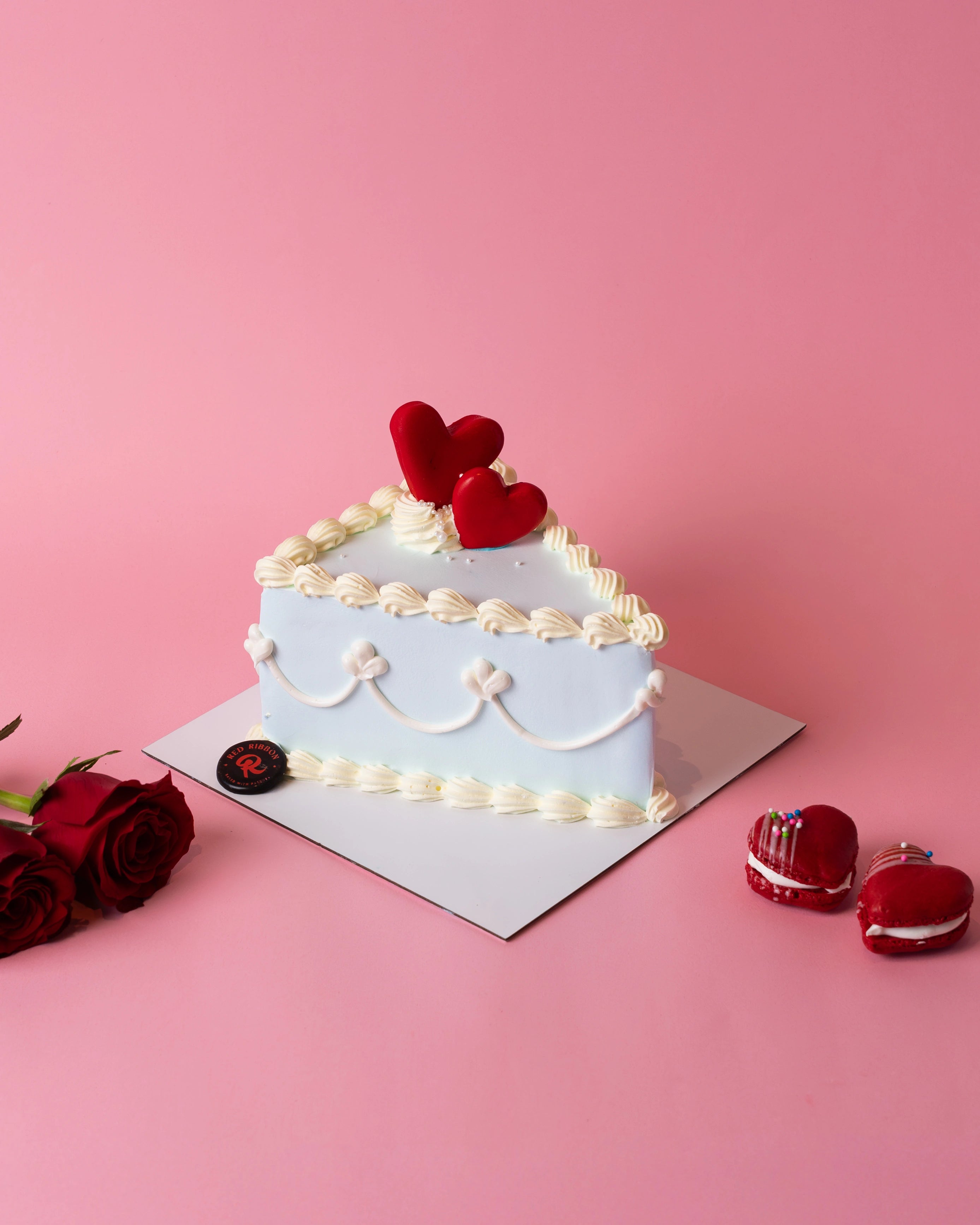 A slice of the Valentine Bento Cake, the best cake in Dubai for intimate celebrations, decorated with light blue frosting, white piping, and red heart toppers.