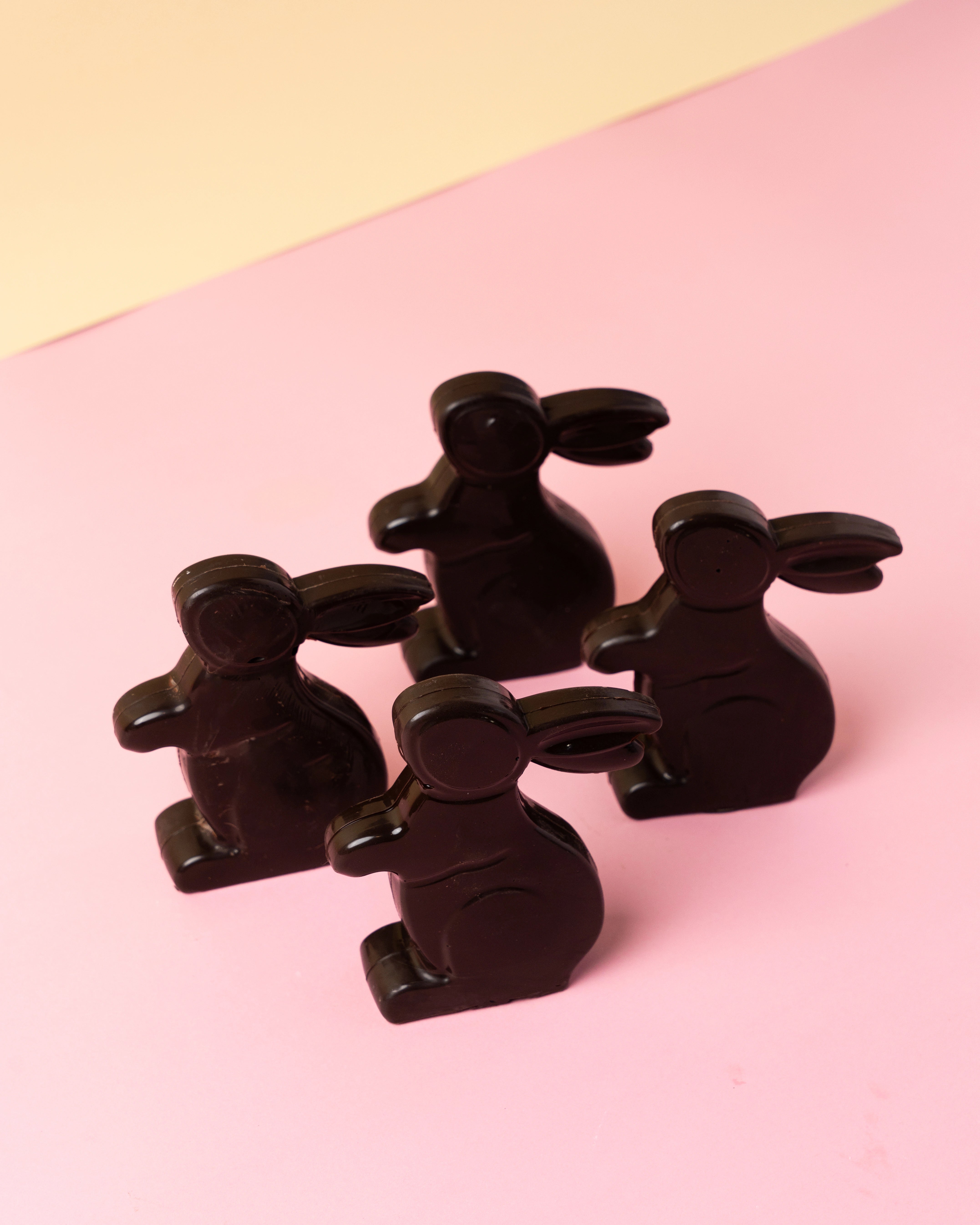 easter chocolate bunny shapes made from dark chocolate arranged on pastel pink surface with soft yellow background, festive treats from red ribbon cakes & bistro dubai