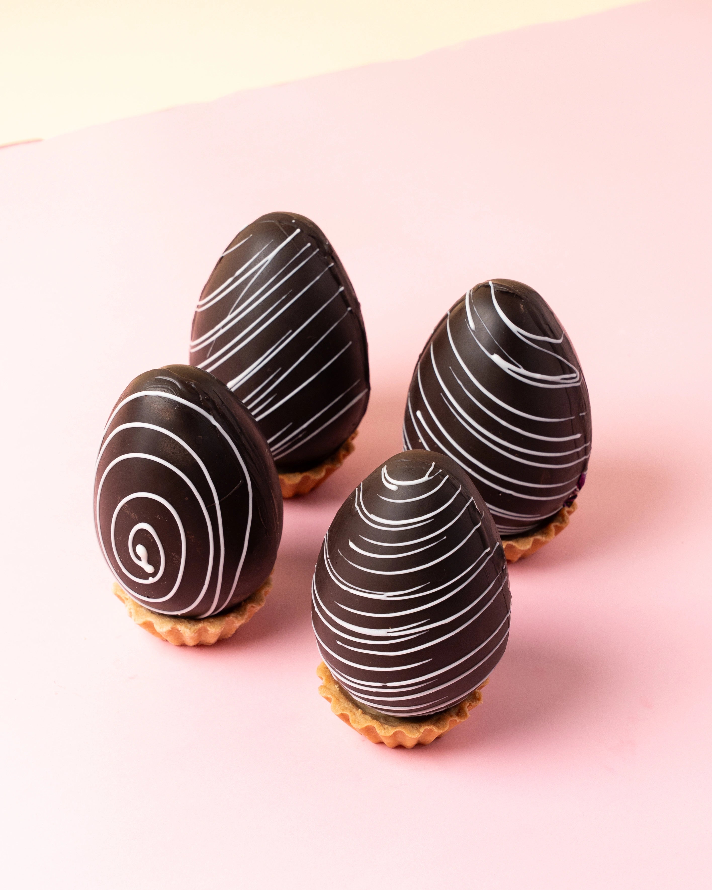 easter chocolate eggs with dark chocolate shell and white drizzle design on soft pink background, premium festive treats from red ribbon cakes & bistro dubai