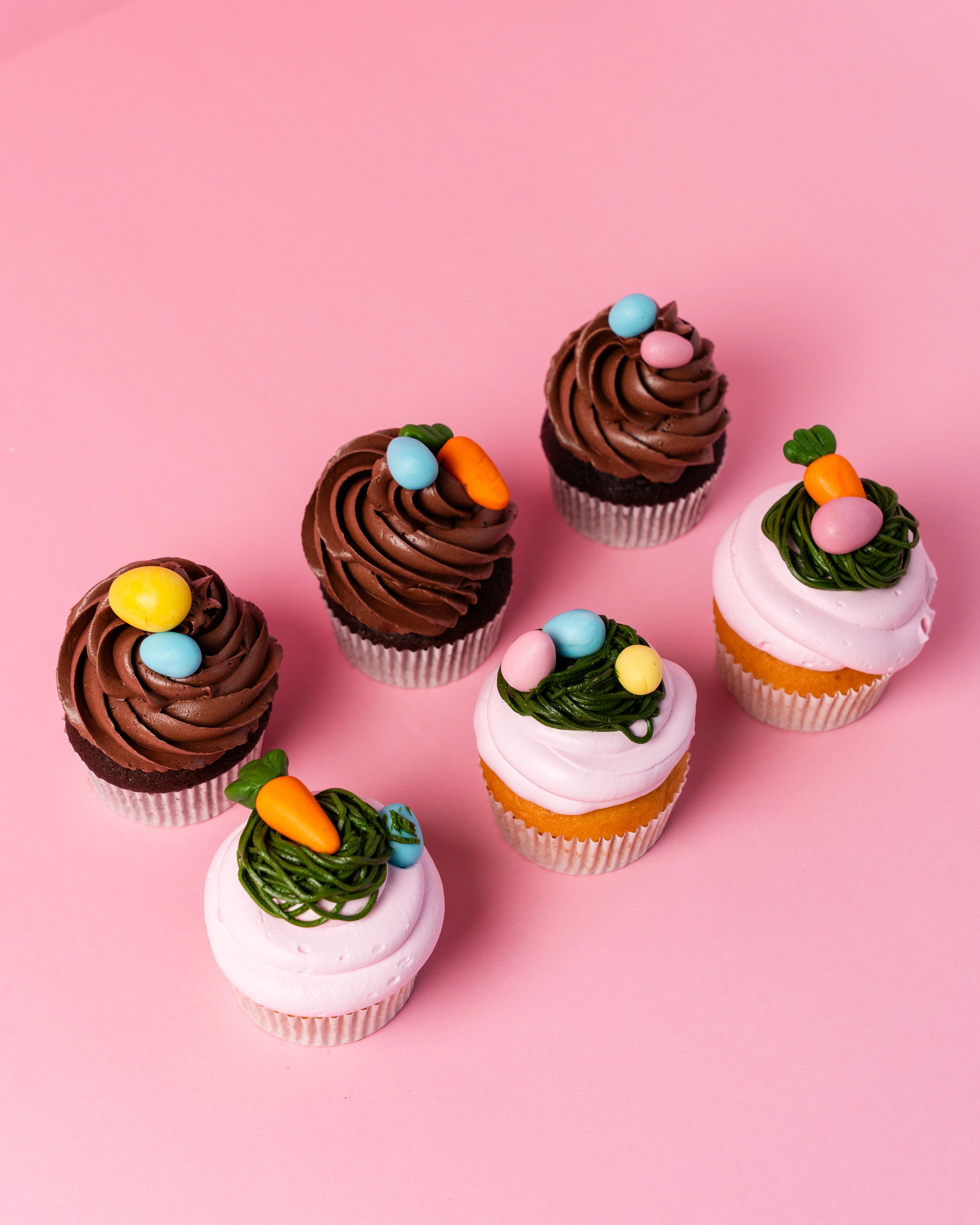 easter cupcakes bundle with chocolate and vanilla cupcakes decorated with mini eggs, carrots, and festive icing on pink background, red ribbon cakes & bistro dubai